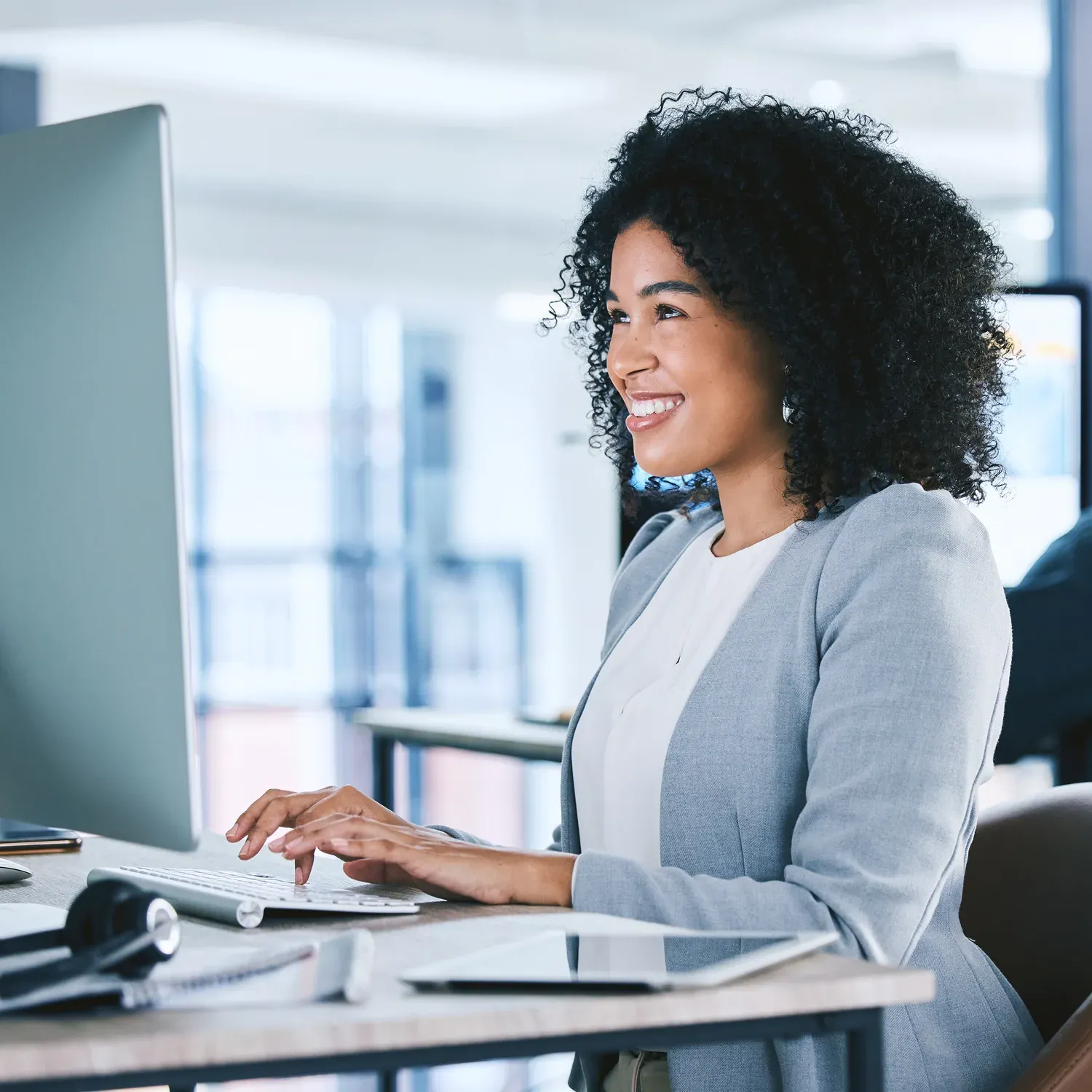 Mulher sorridente trabalhando no computador em um escrit&oacute;rio.