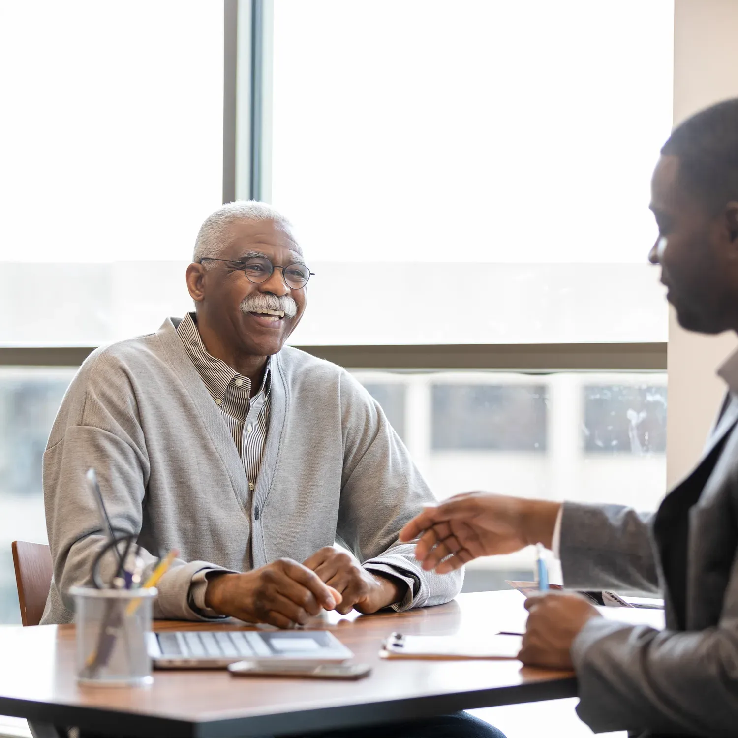 Homem idoso negro sorridente em atendimento presencial com um consultor.
