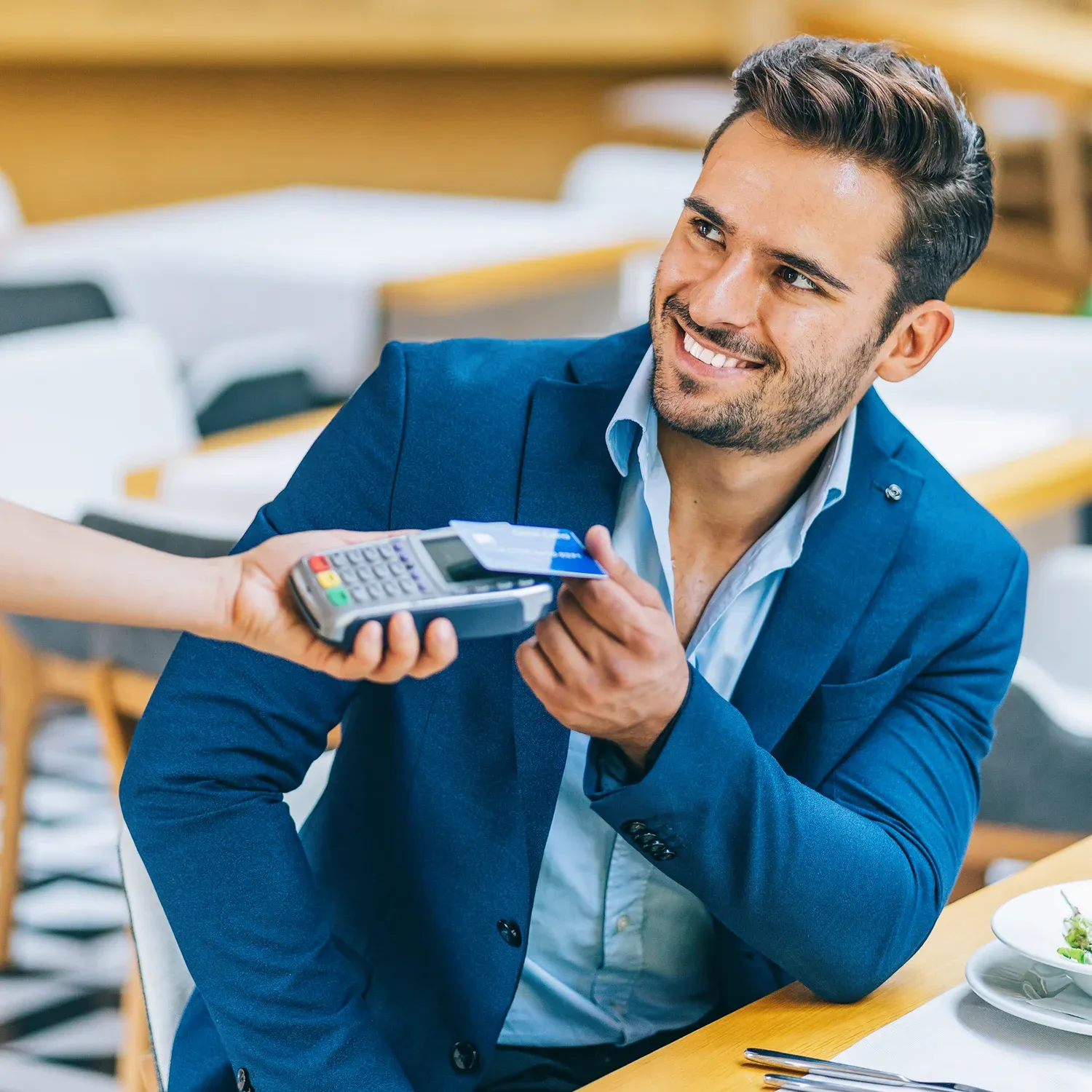 Homem sorridente realizando pagamento por aproxima&ccedil;&atilde;o com cart&atilde;o em restaurante.