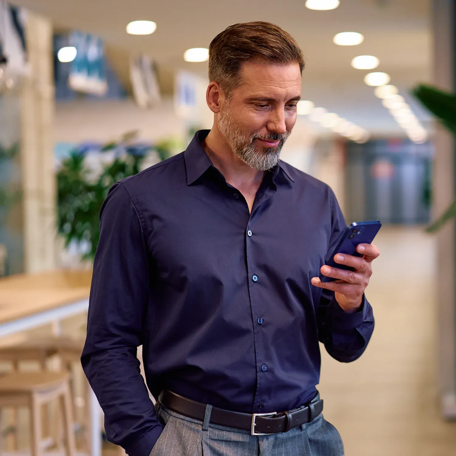 Homem grisalho sorridente usando o celular no escrit&oacute;rio.