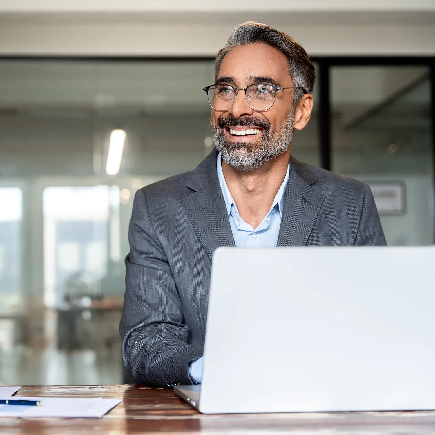 Executivo grisalho sorridente trabalhando no notebook em ambiente corporativo.