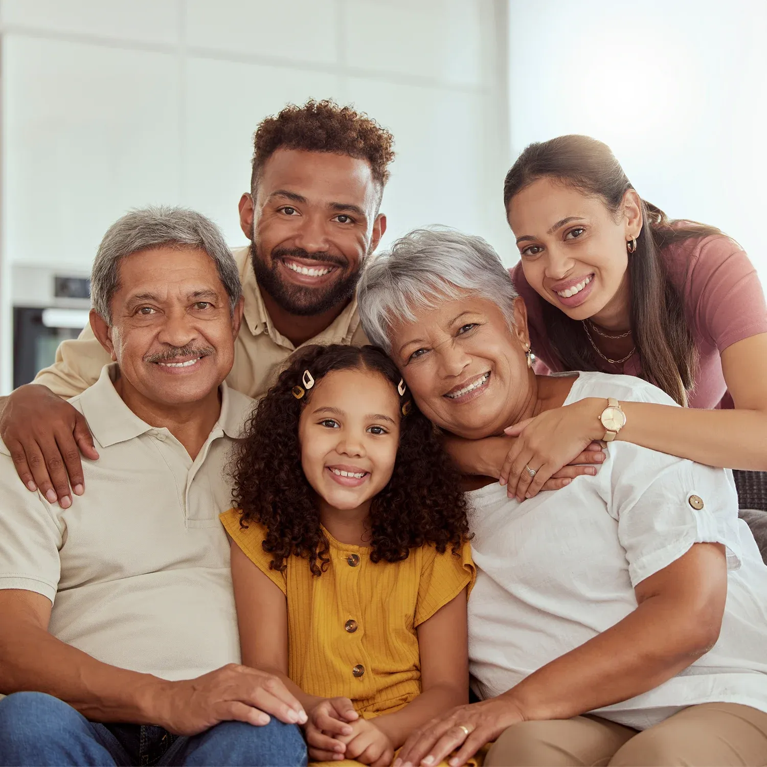 Retrato familiar com av&oacute;s, pais e uma crian&ccedil;a sorrindo juntos em um ambiente residencial.