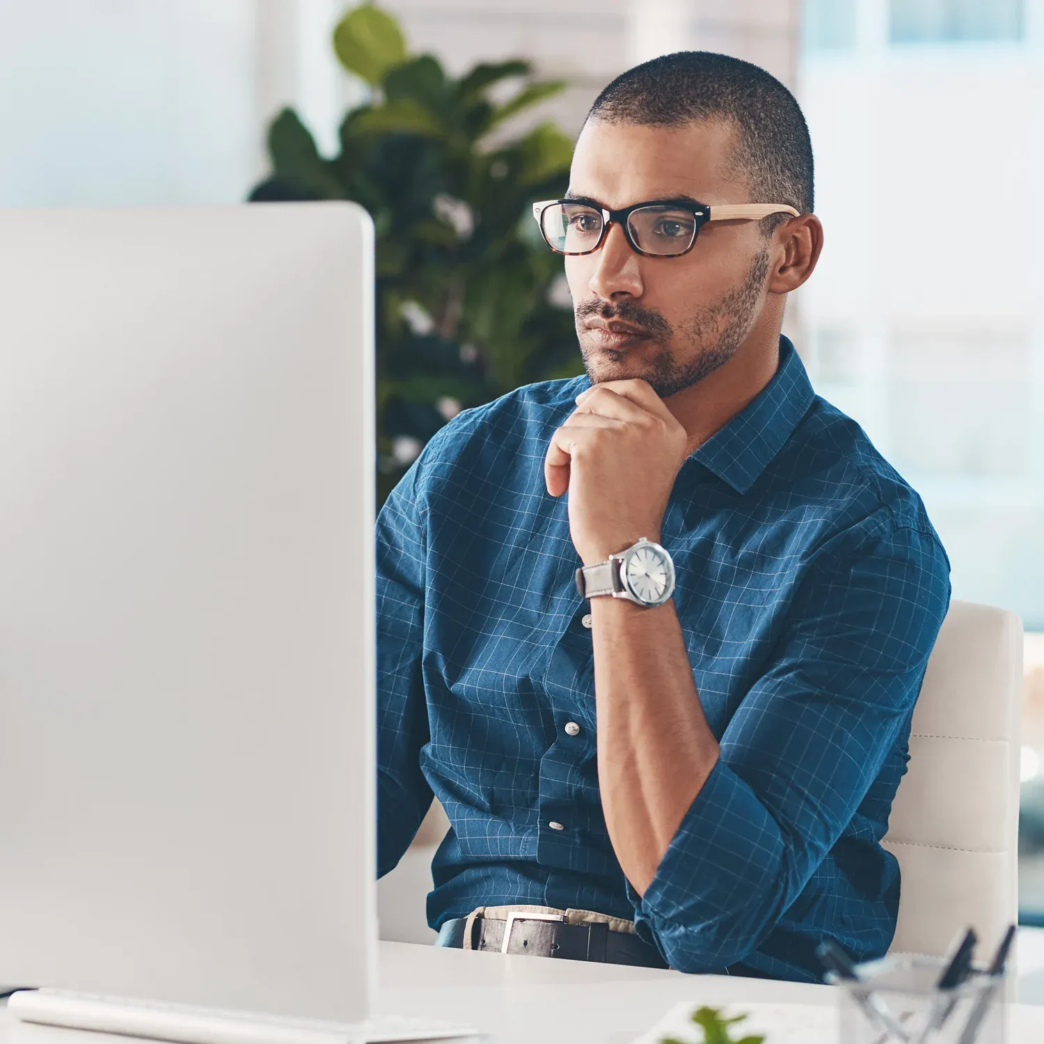 Homem de &oacute;culos pensado e focado diante do computador no escrit&oacute;rio.