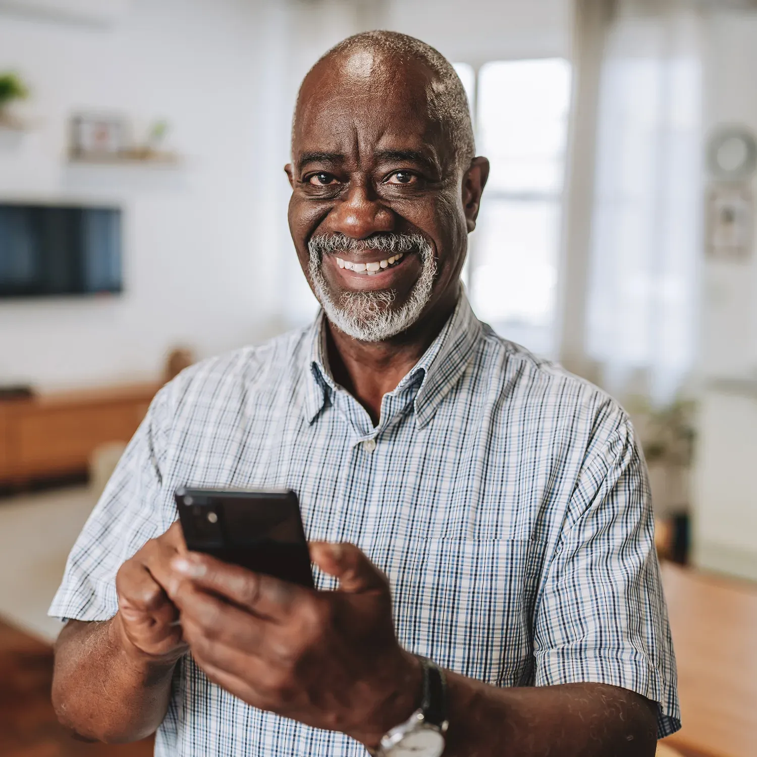 Idoso negro sorridente olhando para a c&acirc;mera com o celular na m&atilde;o.